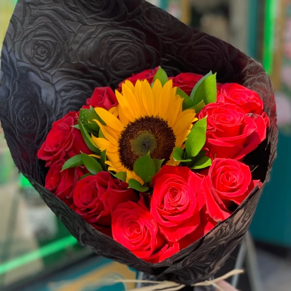 Bouquet of red roses with a yellow sunflower wrapped in black paper
