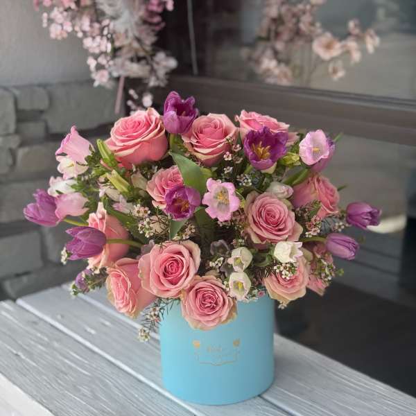 Pink roses and purple tulips arranged in a blue hat box