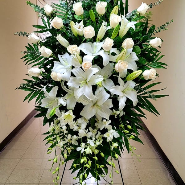 Tall standing spray of white roses, lilies, and orchids on an easel.