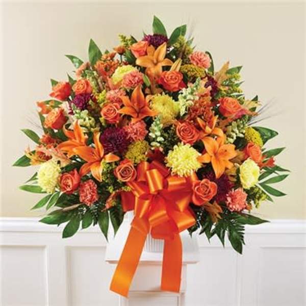 Orange and yellow mixed flower arrangement with a large ribbon in a white vase