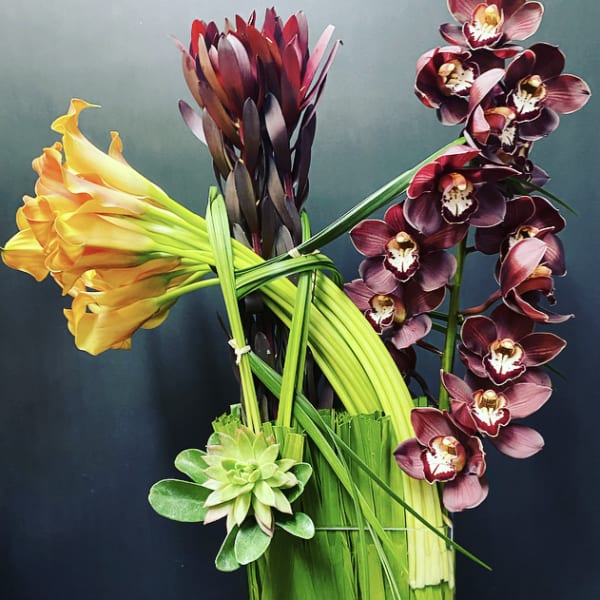 Arrangement of orchids, calla lilies, and a succulent in a tall vase