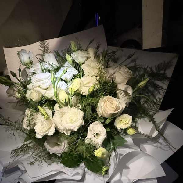 Bouquet of white roses and white lisianthus wrapped in white paper