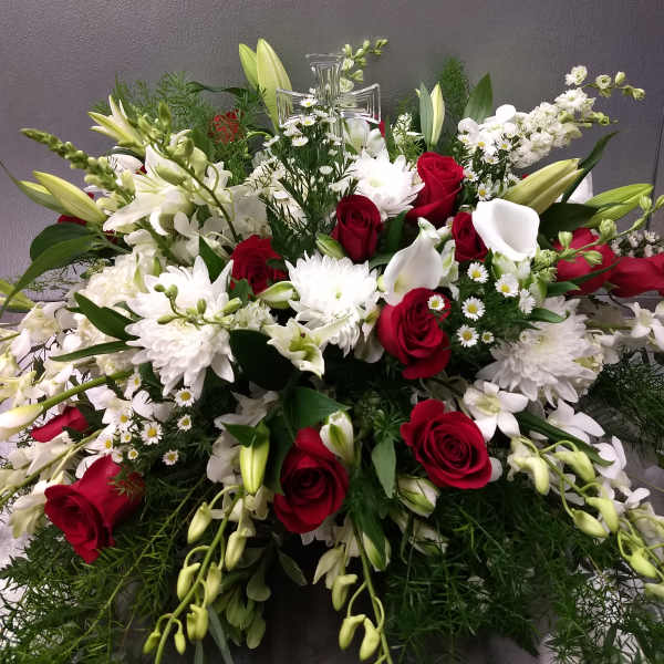 Large red and white floral spray with lilies, roses, and a clear cross topper