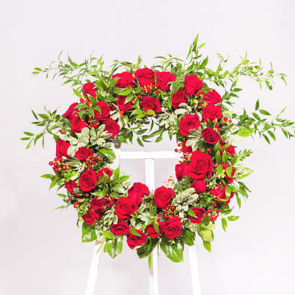 Heart-shaped wreath of red roses and greenery on a white stand