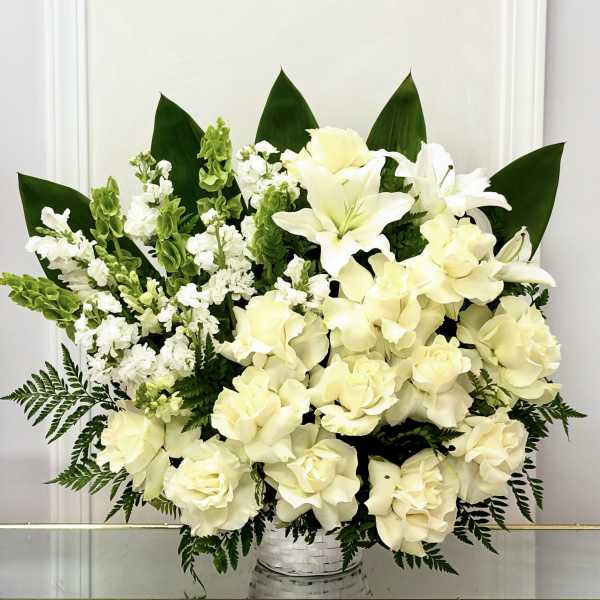 White floral arrangement in a woven basket with dark green leaves