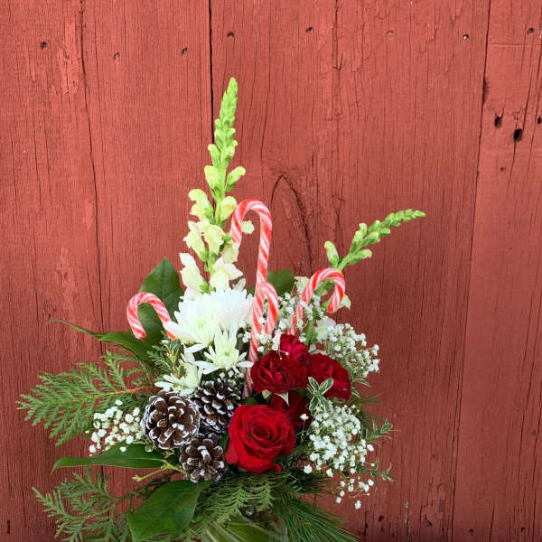 Christmas bouquet with red roses, white blooms, and candy canes in a glass vase
