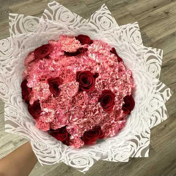 Pink carnation bouquet with red roses wrapped in white patterned paper
