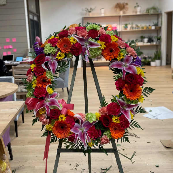 Colorful floral wreath on a metal stand with pink ribbon