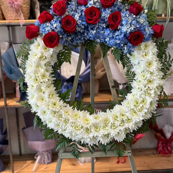 Heart-shaped floral wreath with red roses, blue hydrangeas, and white chrysanthemums
