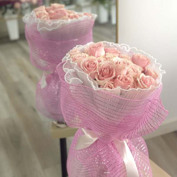 Bouquet of pale pink roses wrapped in pleated white paper and sparkly pink mesh with a ribbon bow