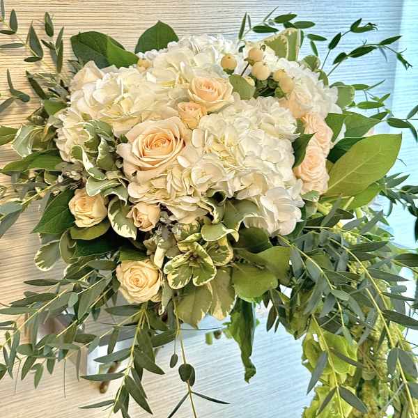 White hydrangeas and peach roses in a lush bouquet with greenery