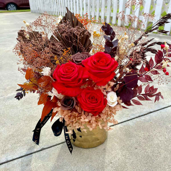 Red roses in a gold vase with dried foliage and berries