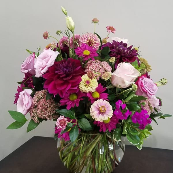 Round arrangement of pink and purple mixed flowers in a clear glass bowl vase