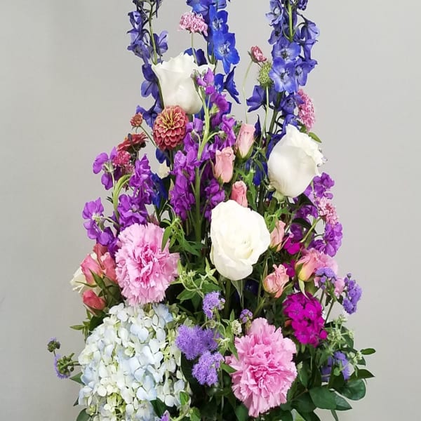 Tall mixed arrangement of purple, pink, blue, and white flowers in a white vase on a dark table