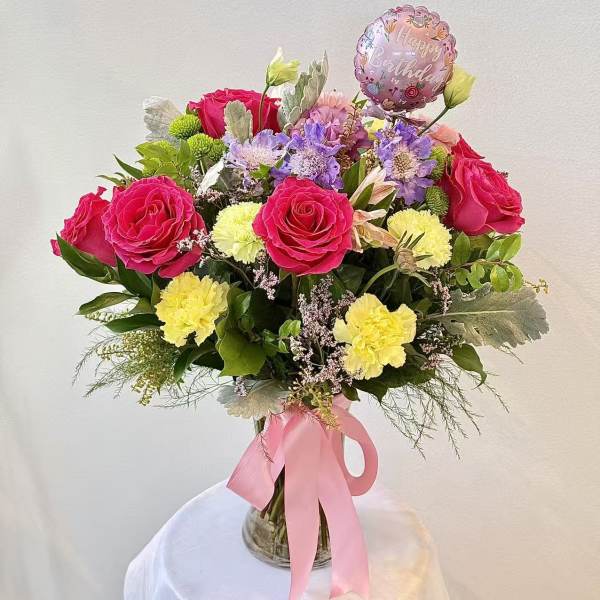Pink rose bouquet with carnations and a birthday balloon in a glass vase