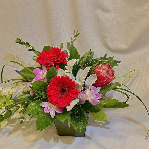 Red gerbera daisies and pink orchids in a low rectangular vase