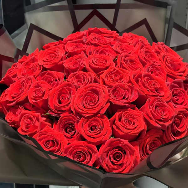 A large bouquet of red roses wrapped in dark paper
