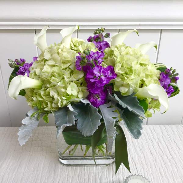 Arrangement of green hydrangeas, purple stock, and white calla lilies in a glass vase