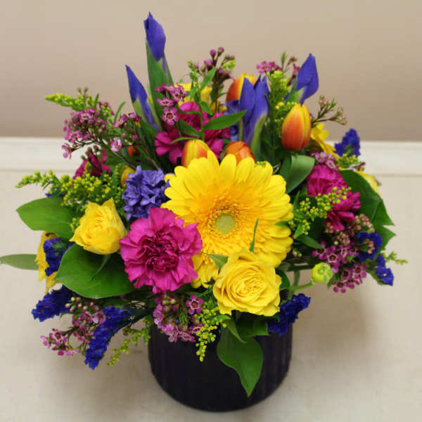 Bright mixed bouquet in a black vase with yellow, pink, and blue flowers