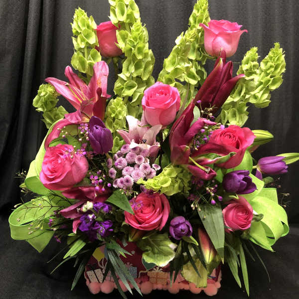 Bright pink roses and lilies arranged with green bells of Ireland in a gift box