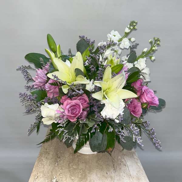 Bouquet of lilies, roses, and white filler flowers in a white vase