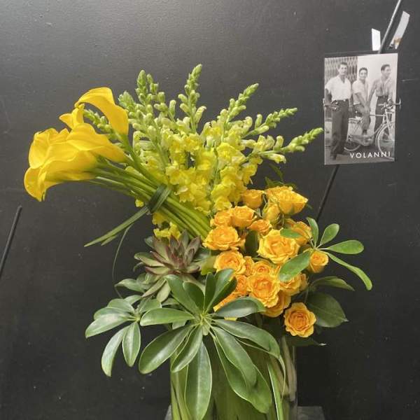 Yellow calla lilies and roses in a glass vase with greenery