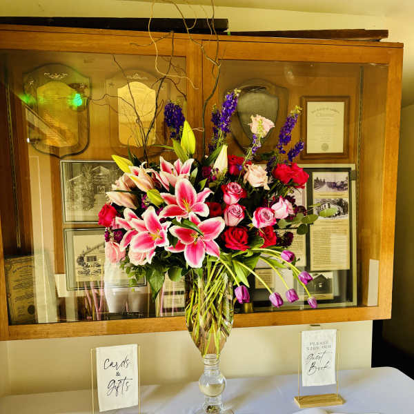 Tall vase arrangement with pink lilies and red roses on a table
