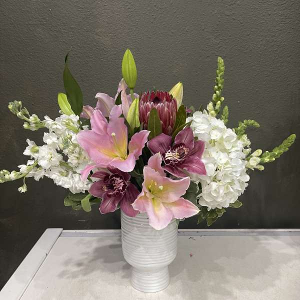 Pink lilies and white blooms arranged in a white vase