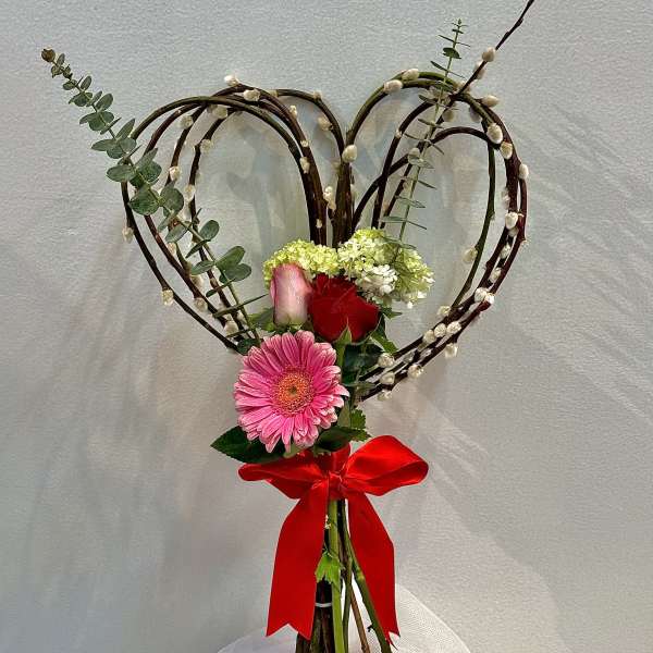 Heart-shaped floral arrangement with roses, gerbera daisy, and a red ribbon