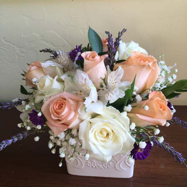 Arrangement of peach and white roses with purple accents in a ceramic vase