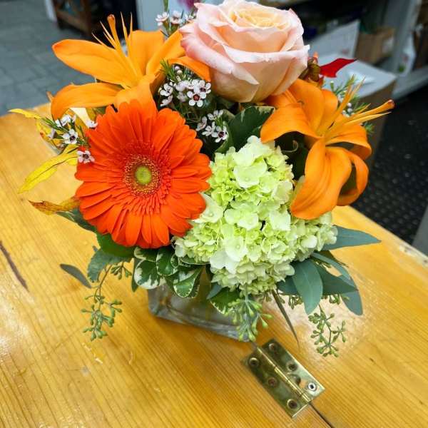 Orange gerbera, peach rose, and green hydrangea arrangement in a glass vase