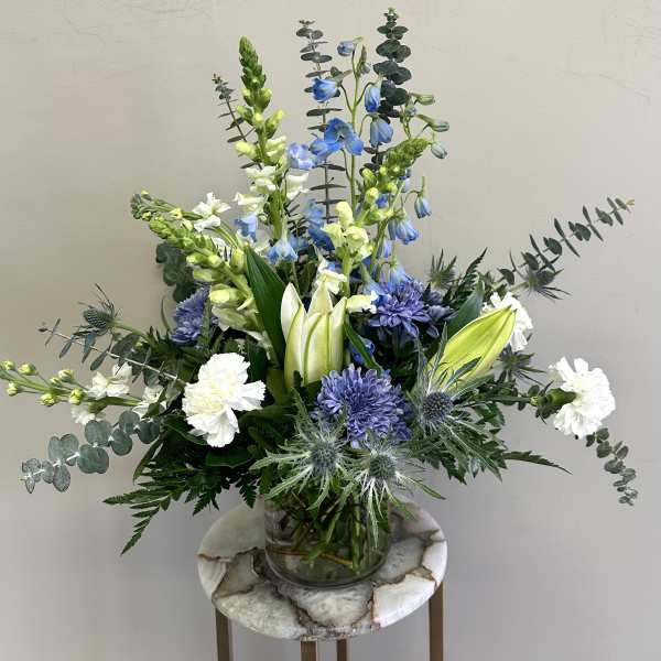 Arrangement of blue and white flowers with lilies and carnations in a clear glass vase