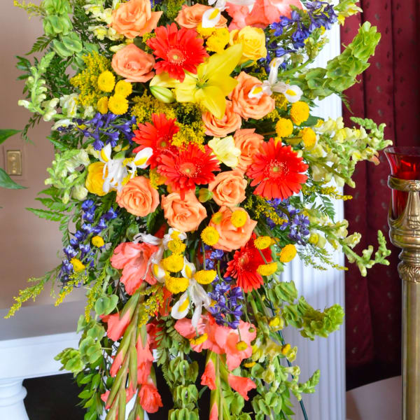 Tall floral standing spray with orange, yellow, purple, and white blooms