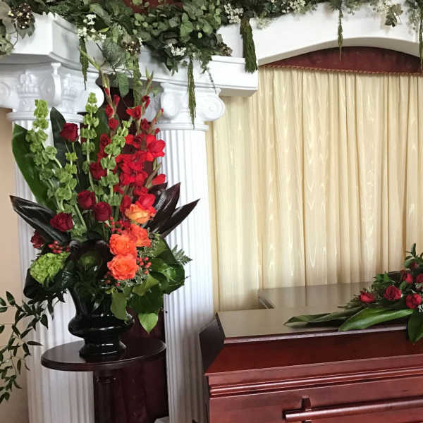 Red and orange floral sprays around a casket in a funeral setting