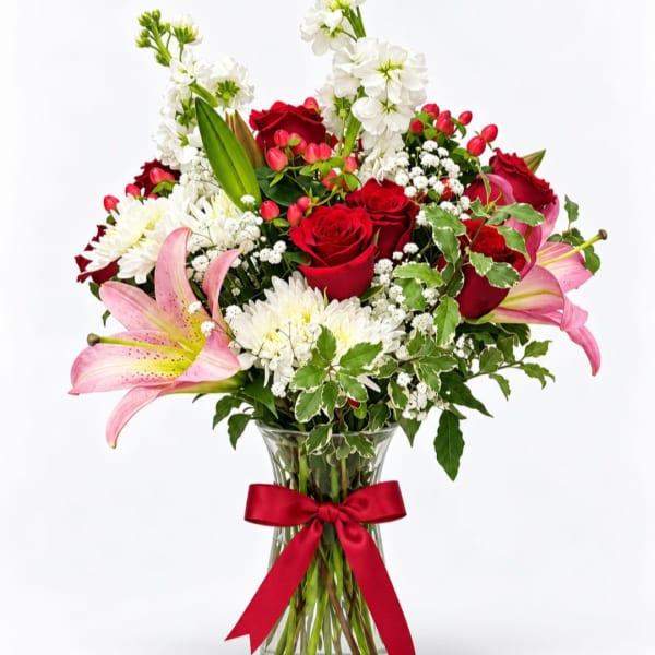 Bouquet of red roses, pink lilies, and white flowers in a glass vase with a red ribbon