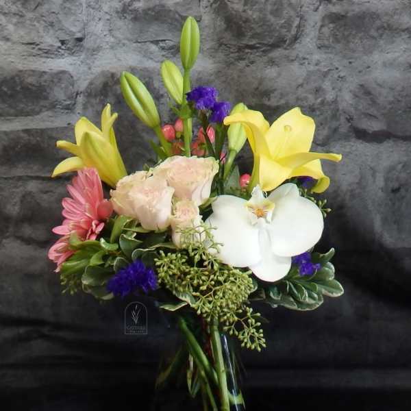 Mixed bouquet with yellow lilies, white orchid, pink blooms, and pale roses in a glass vase