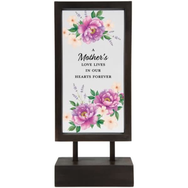 Framed floral memorial sign on a dark stand with the words "A Mother's Love Lives in Our Hearts Forever"