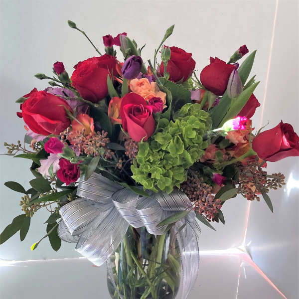 Bouquet of red roses and mixed flowers in a glass vase with a silver ribbon