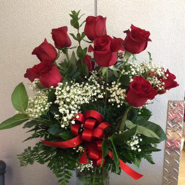 Red roses arranged in a clear glass vase with baby's breath and a red ribbon