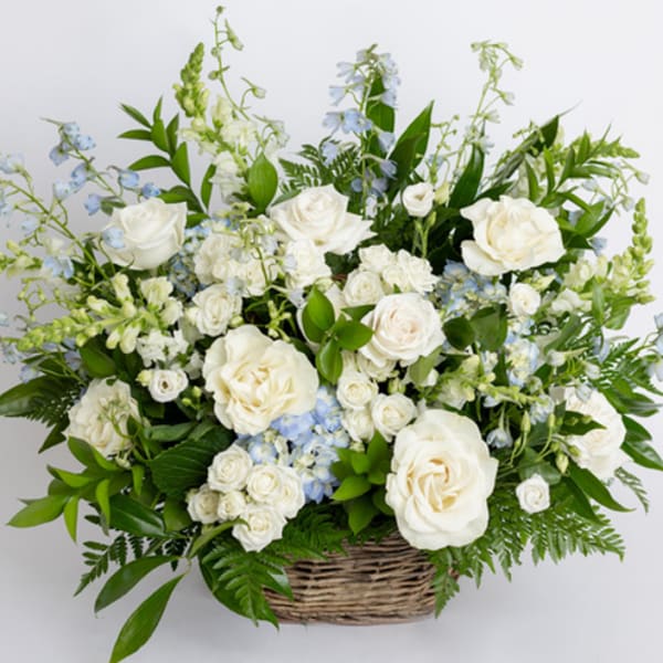 Large white and pale blue flower arrangement with roses in a wicker basket
