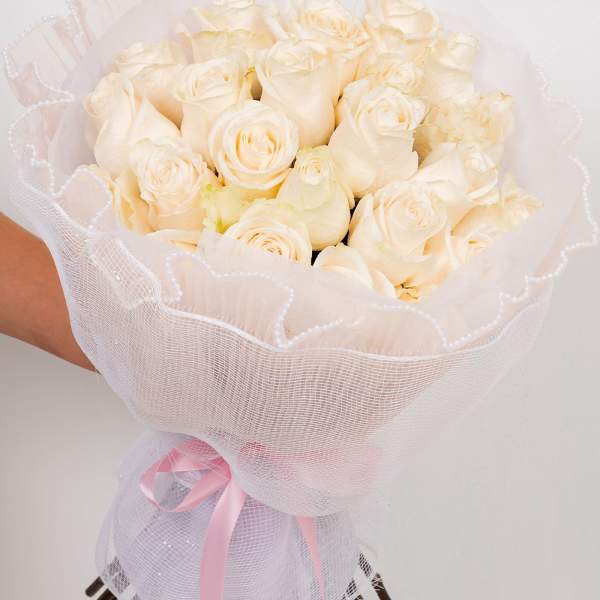 Bouquet of cream roses wrapped in white mesh with a pink ribbon