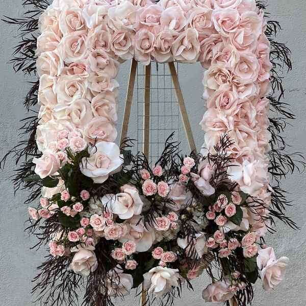 Large pale pink floral wreath on a stand with dark foliage accents