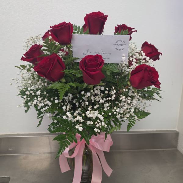 Red roses arranged in a glass vase with baby's breath and a pink ribbon