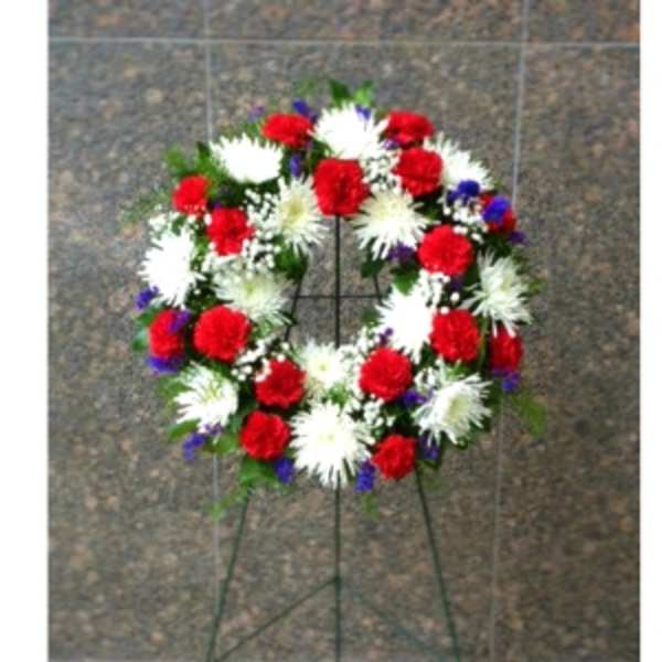 Standing wreath of red carnations and white mums with blue accents on a metal easel
