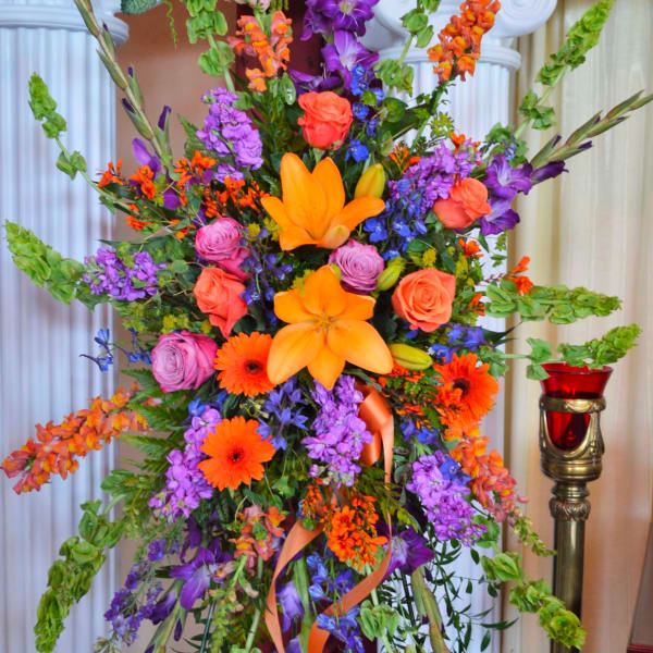 Tall floral standing arrangement with orange, purple, and pink blooms