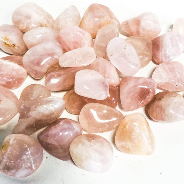 Pile of polished pink and peach tumbled stones on a white surface