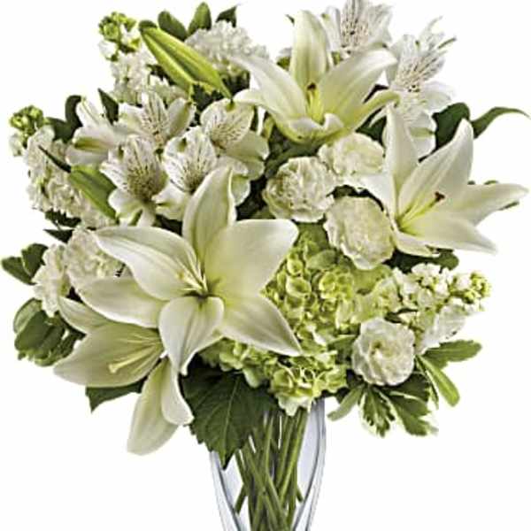 White lilies and mixed white flowers in a clear glass vase