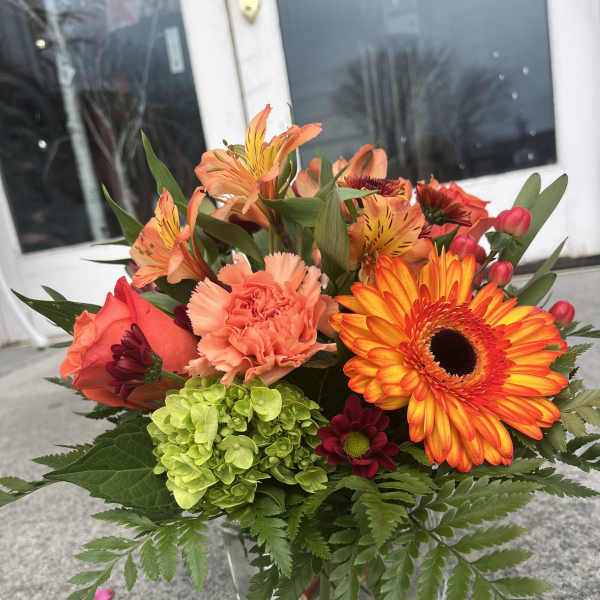 Mixed bouquet in a clear glass vase with orange and coral blooms