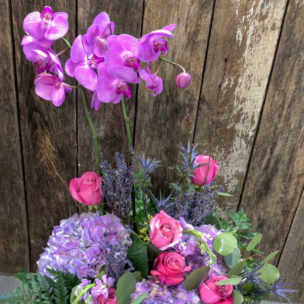 Pink orchids and roses arranged with lavender hydrangeas in a basket