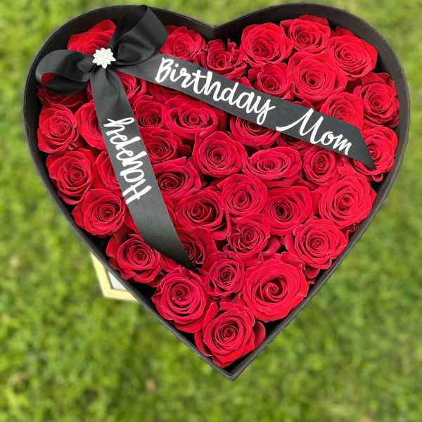 Heart-shaped box of red roses with a black ribbon reading Birthday Mom